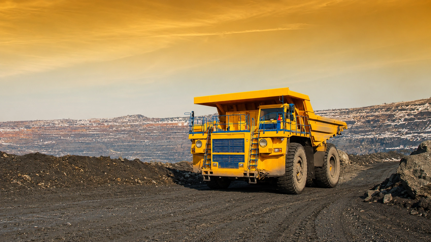 Large yellow mining dump truck operating on a haul road inside a terraced open-pit mine.